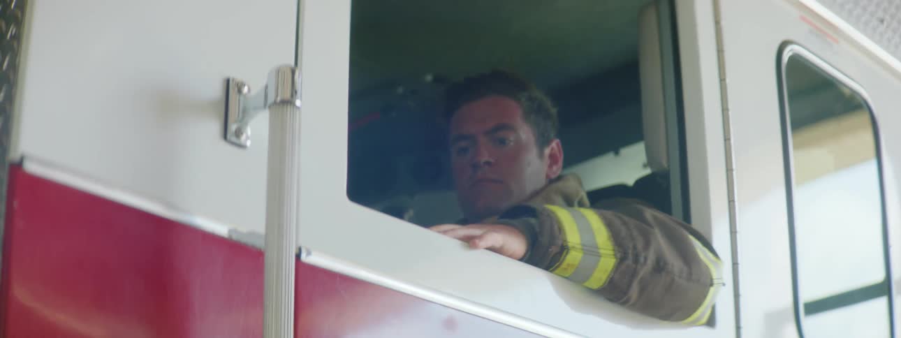 A firefighter wearing protective gear sits in fire engine and closes door