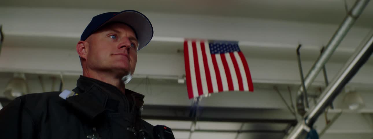 Firefighter stands proud under a united states flag inside a fire station