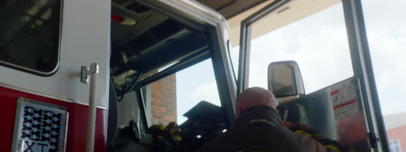 Firefighter gearing up and boarding a fire truck parked in a fire station