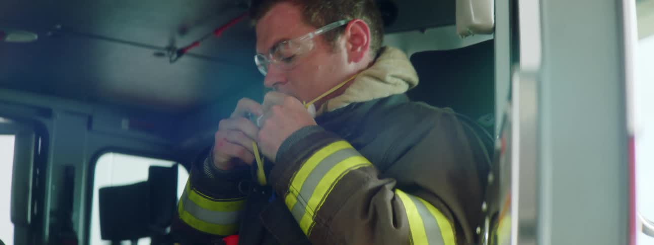 Firefighter sitting inside a fire truck puts a face mask on