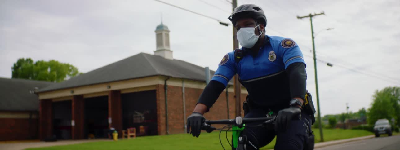 Police officer with a black helmet and a face mask rides a bicycle on a road