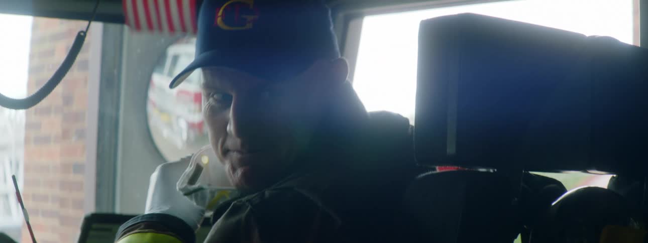 Man sitting in passenger seat looks over shoulder to talk as fire engine is reflected in mirror seen through windshield