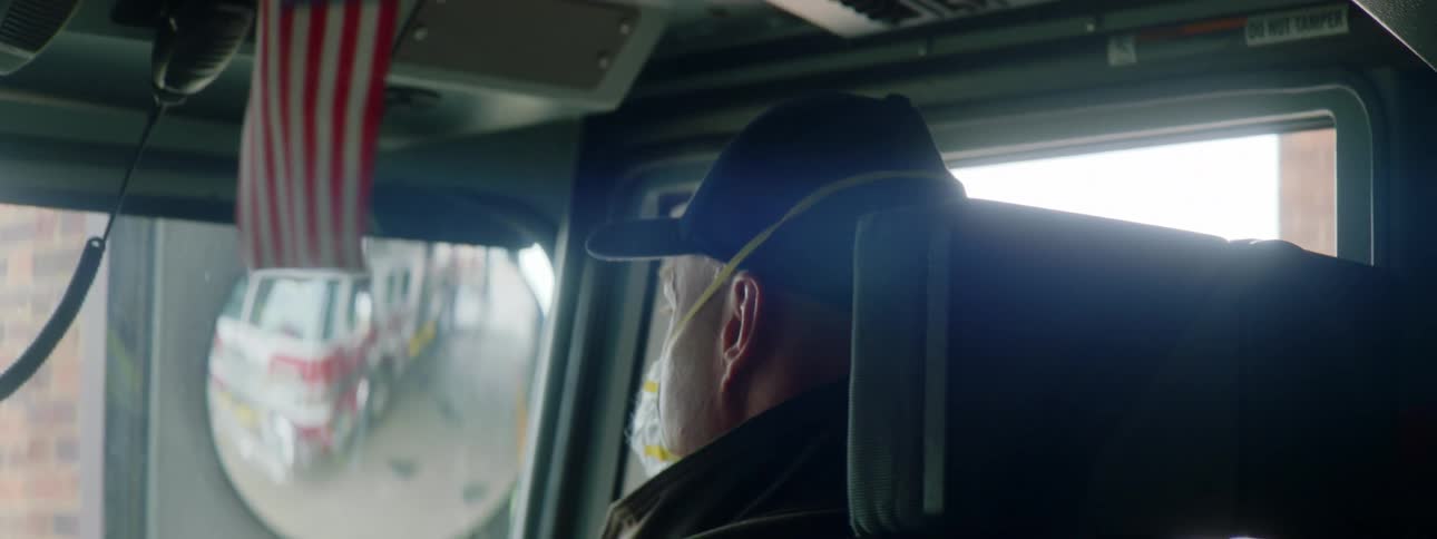 A firefighter in a truck adjusts his mask and looks behind him