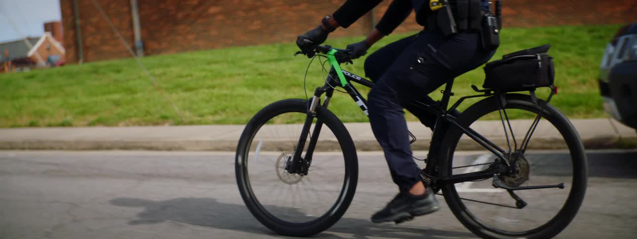 Police officer with a black helmet and a face mask rides a bicycle on a road