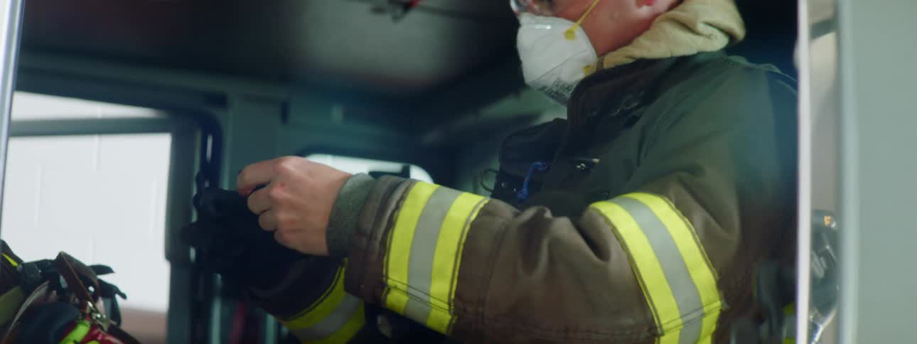 A man is sitting in a firetruck and putting on gloves