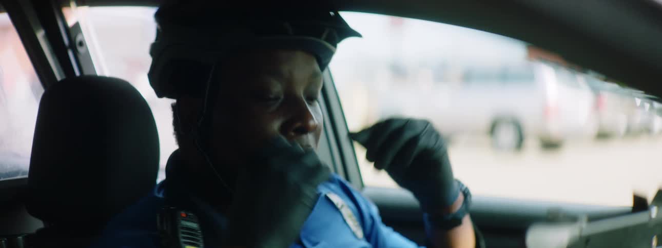 A police office wearing a bicycle helmet adjusts his helmet before climbing out of his police car