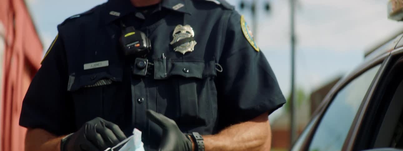 Police officer standing near car parked on street puts on face mask