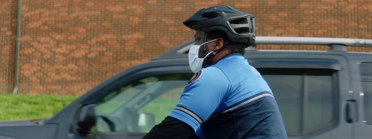 Police officer wearing a face mask rides a bicycle patrolling the neighborhood