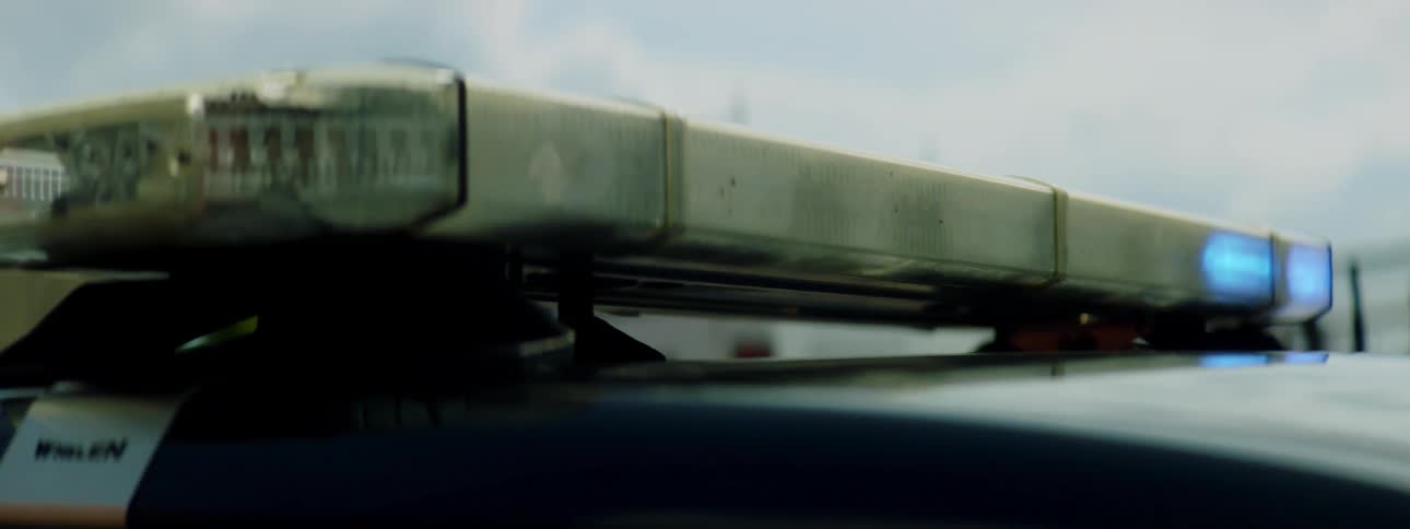 A stationary police car has flashing blue lights continuously blinking atop its roof