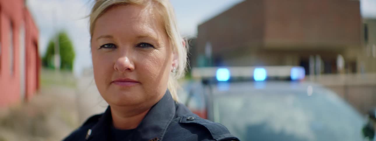 Close up of a female police officer face in front of a patrol car in the street of a small town