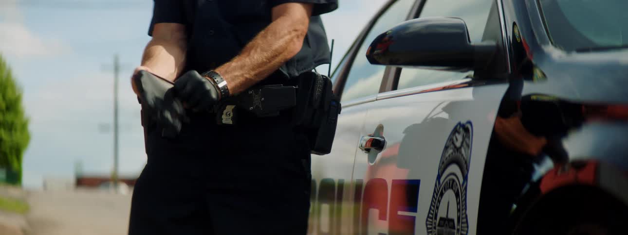 Male police officer dons black latex gloves standing near police car