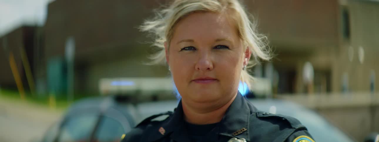 Close up of a female police officer face on a windy day in front of a patrol car with flashing blue lights