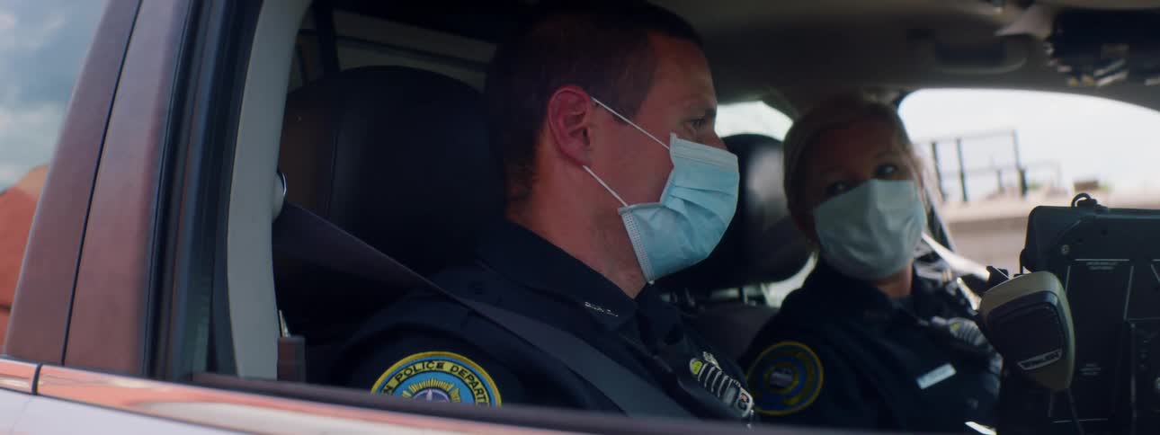 A male and female officer wear masks as they sit in their vehicle and talk