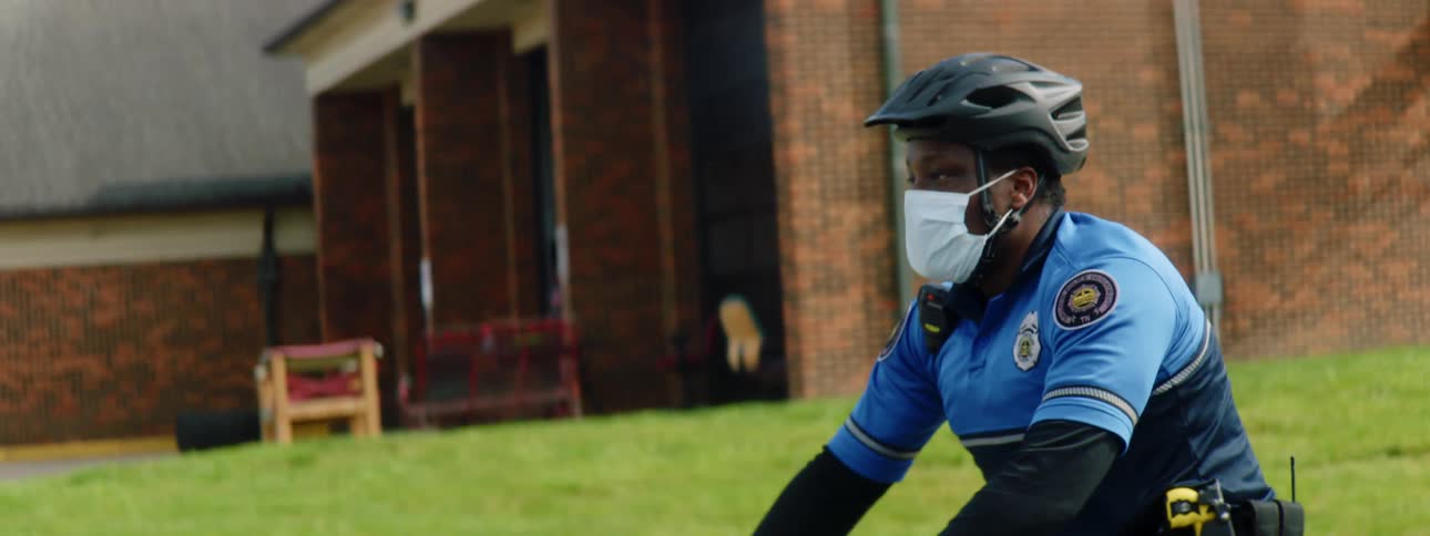 A police officer wearing a medical mask rides a bicycle through a neighborhood during the day