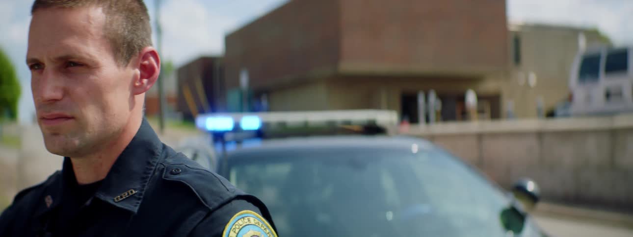 A police officer is standing outdoors by a police car