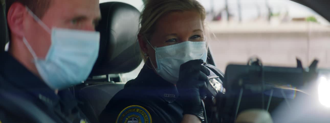 A male and female police officers sitting in a car wearing a mask and gloves