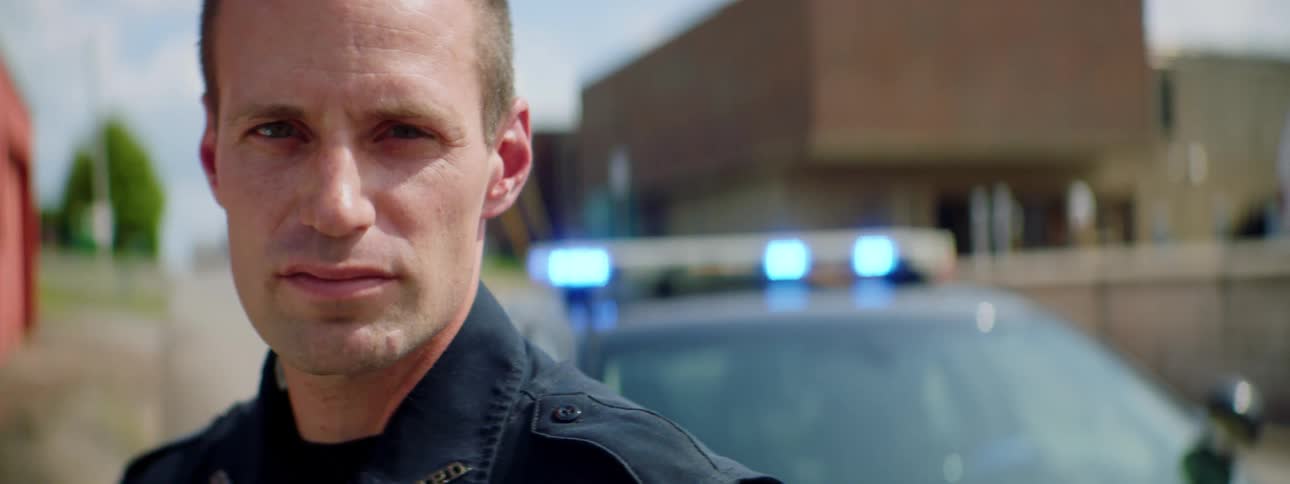 A police officer stands outside of his police car with the lights flashing