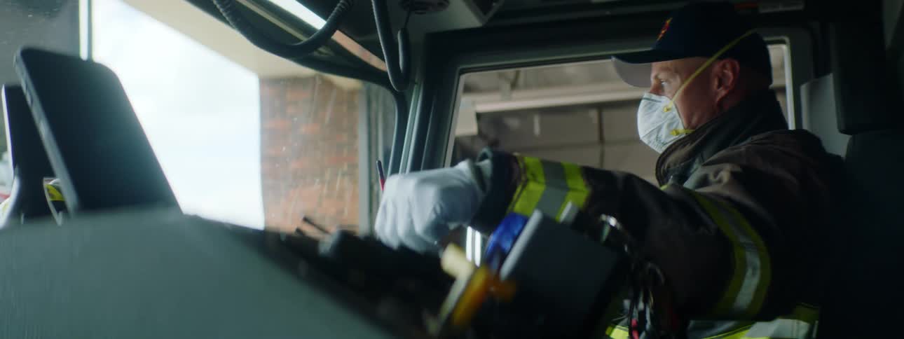 Firefighter puts face mask on while sitting on the passenger seat of a fire truck inside a fire station