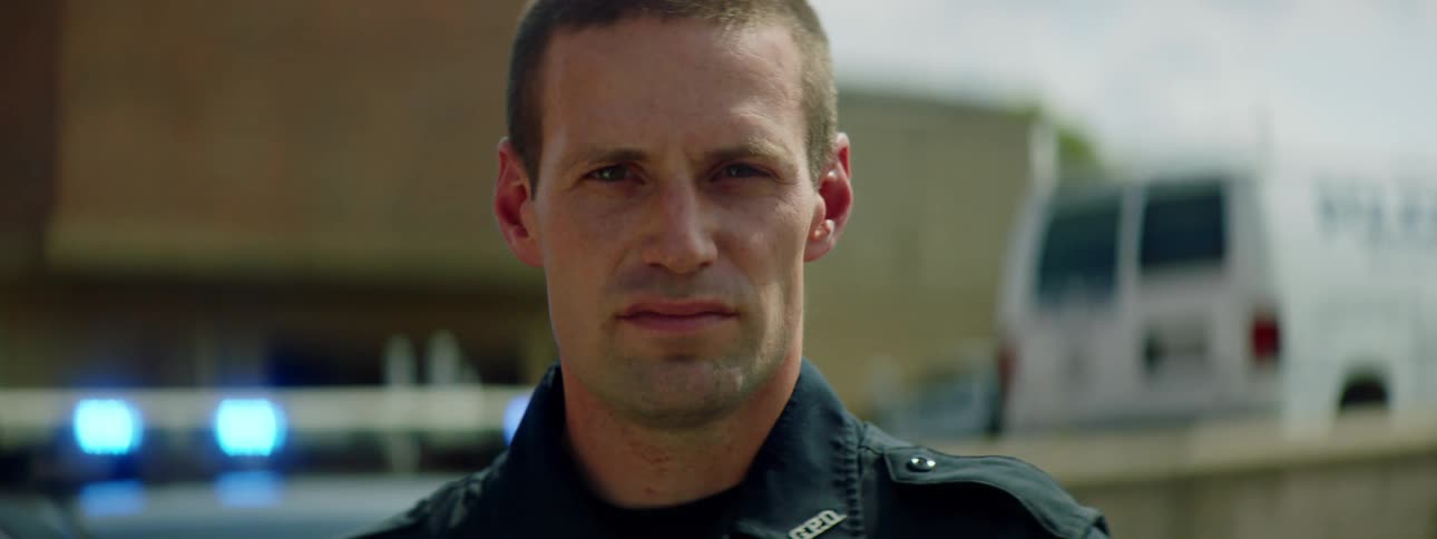 Police officer with a police uniform and standing by a police car and looks at the camera in the street
