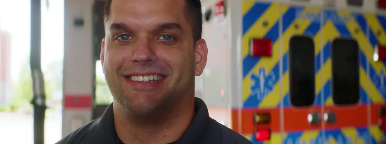 A paramedic smiles as he poses in front of an ambulance