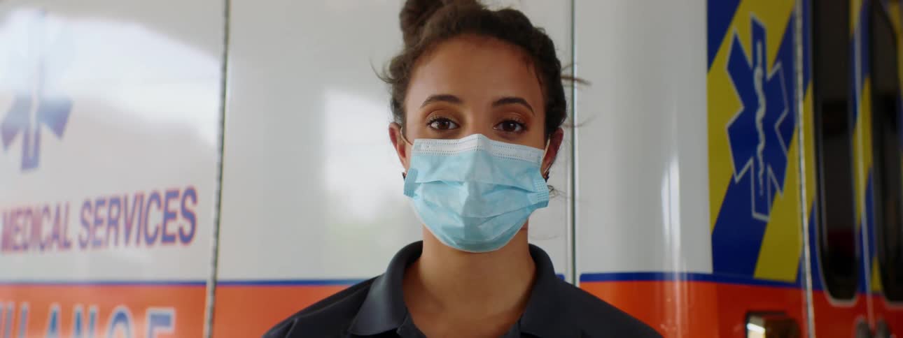 An emergency responder stands in front of an ambulance with a face mask