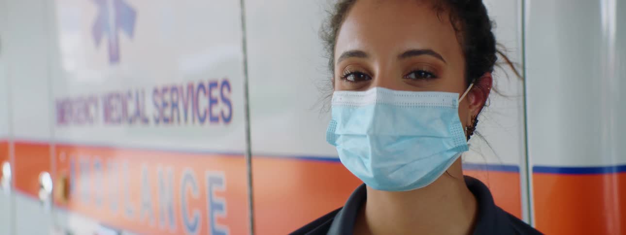 Woman wearing a medical mask stands next to an ambulance