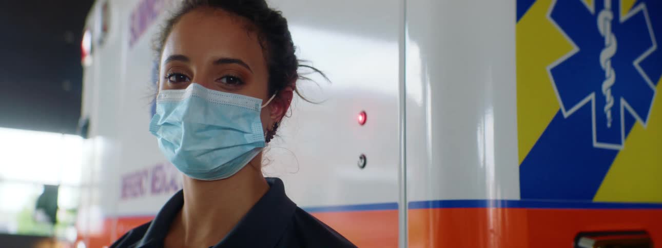 Woman wearing a medical mask stands next to an ambulance