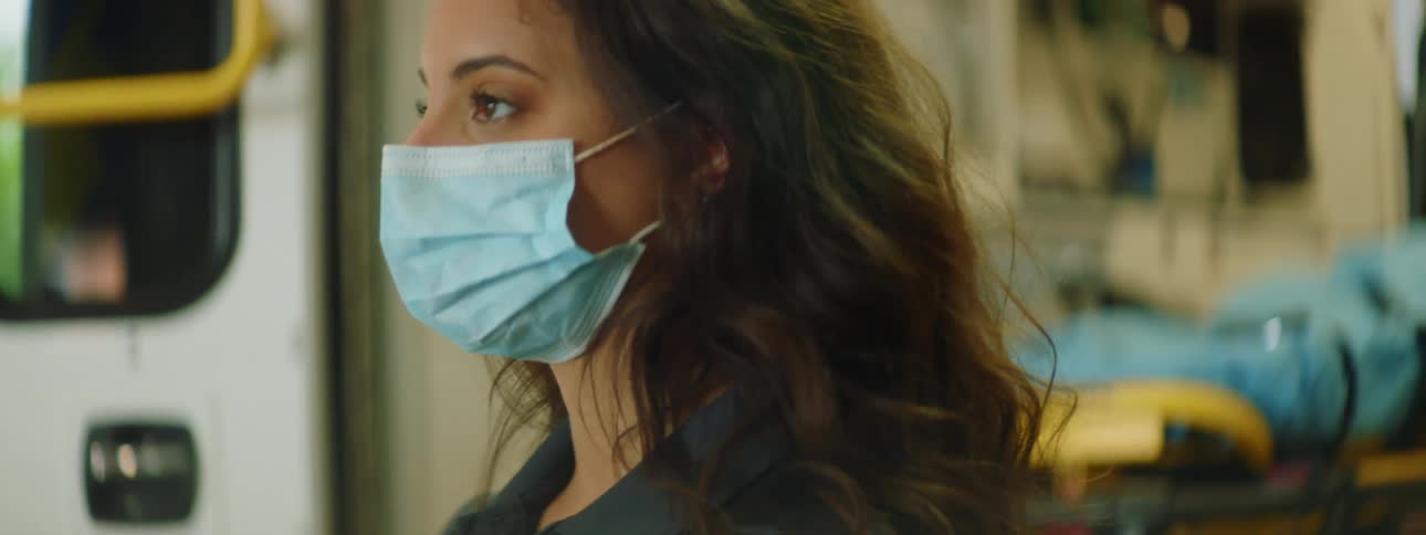 A female paramedic in a medical mask stands outside of an ambulance