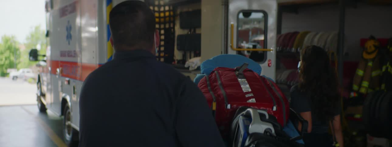 Paramedics carry a stretcher into an ambulance parked on a fire station