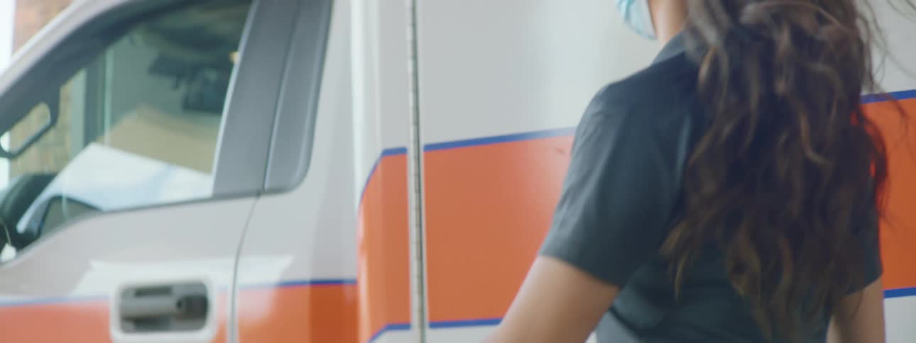 A pair of paramedics close the back doors of an ambulance before the female paramedic walks around the vehicle to enter the drivers seat