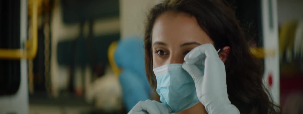 A paramedic standing in front of an ambulance puts a mask on