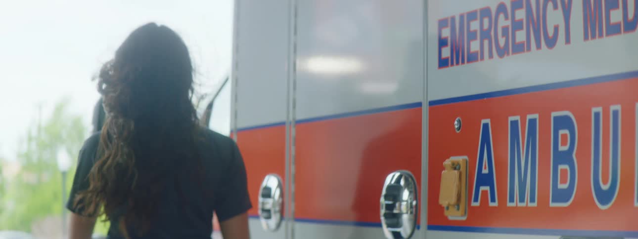 Female paramedic wearing a face mask boards an ambulance on the drivers side