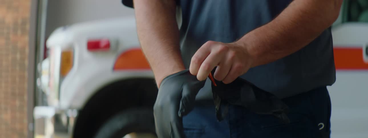 Paramedic puts on black latex gloves in front of an ambulance