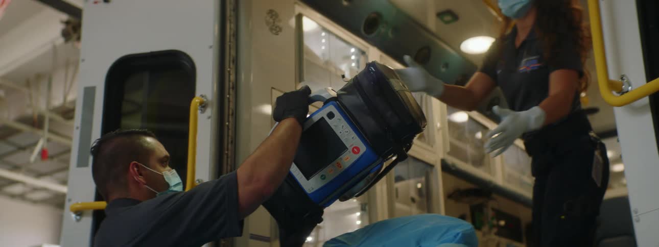 A man and woman with gloves and masks putting bags into an ambulance