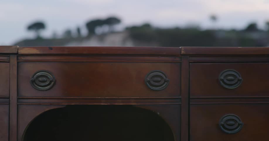 Old wooden desk with drawers sitting in a grass field next to a mountain in the morning