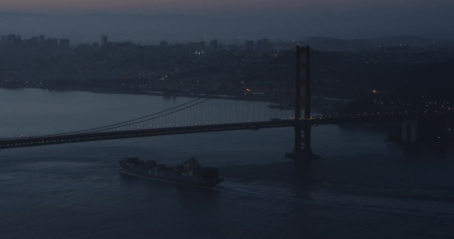 A barge passes under a bridge in new york at dusk