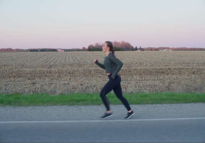 A woman jogs past a dry empty field in the morning