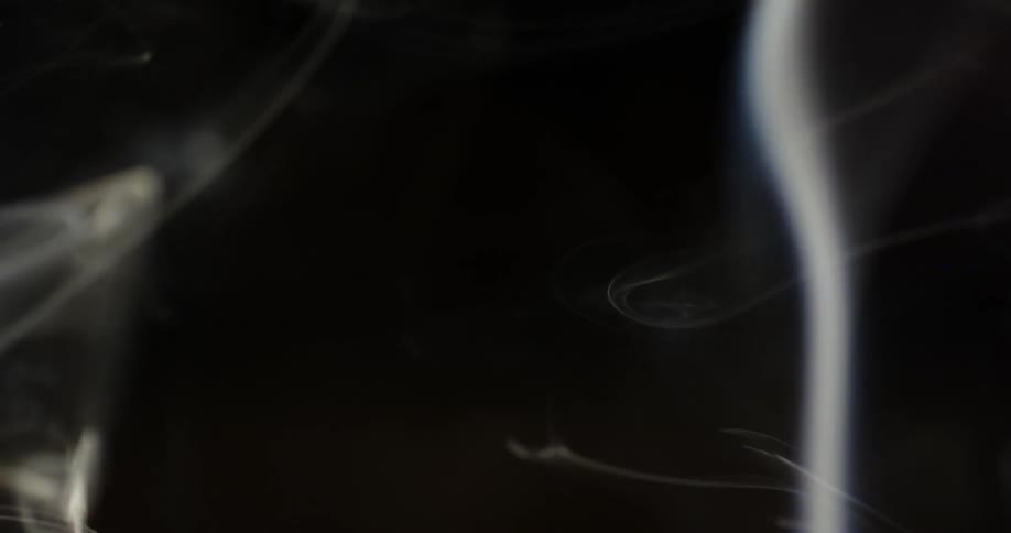 Smoke rises and swirls in a dark area