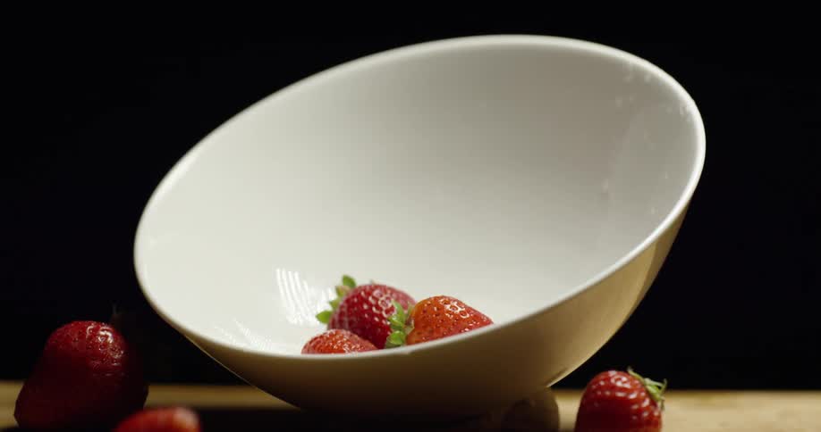 Strawberries fall into a white bowl