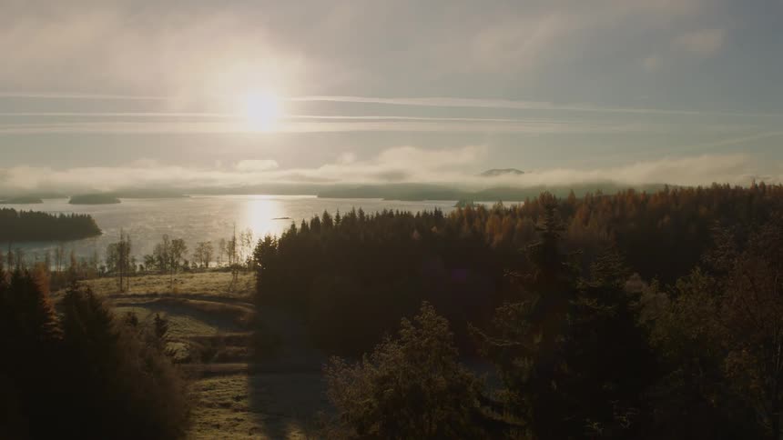 The sun shines over a lake with clouds hovering below