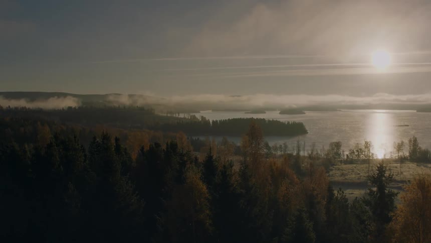 The sun shines over a lake with clouds hovering below