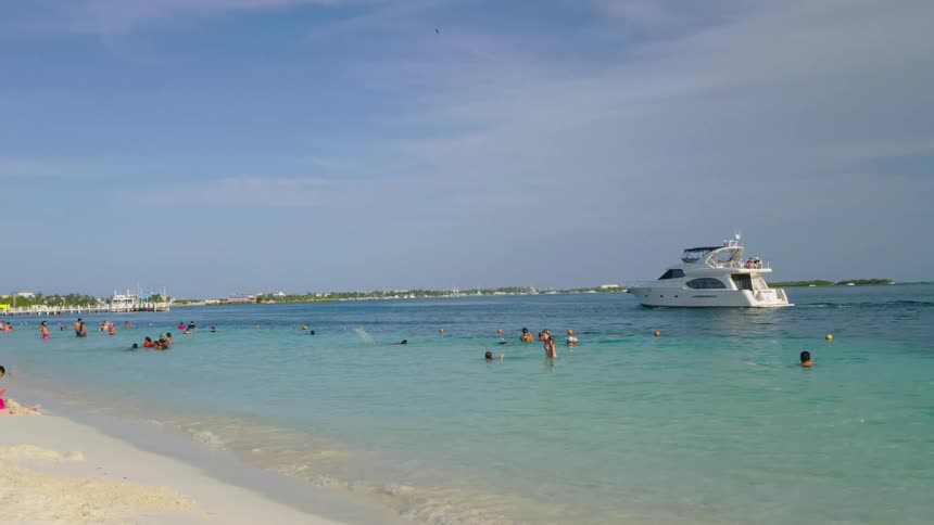 A beach with sand waves and people with boats the sky and clouds in the background