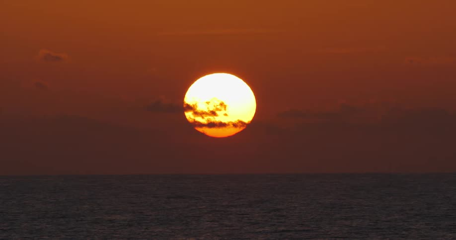 The sun sets over an ocean in an orange sky