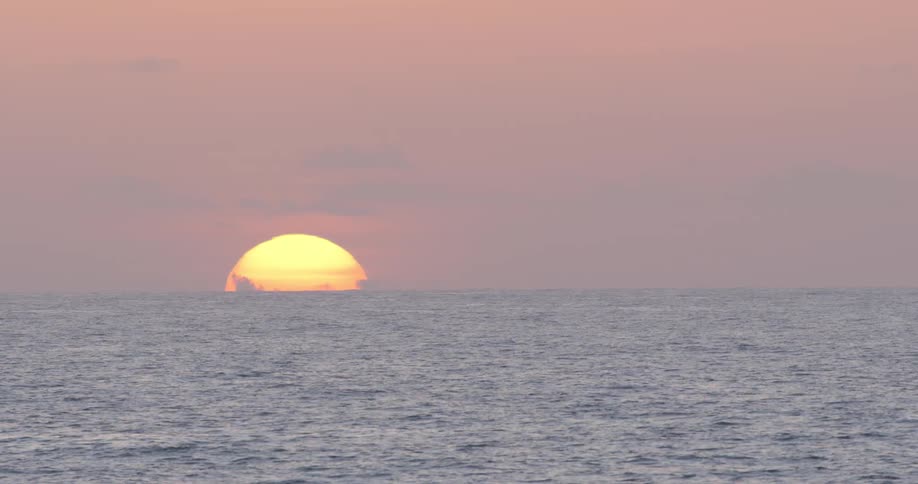 The sun is seen just barely peaking over the horizon of the open ocean