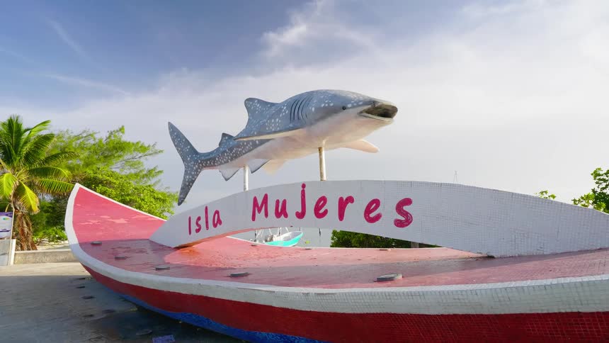 A sign near the coast with trees a boat the ocean and the sky in the background