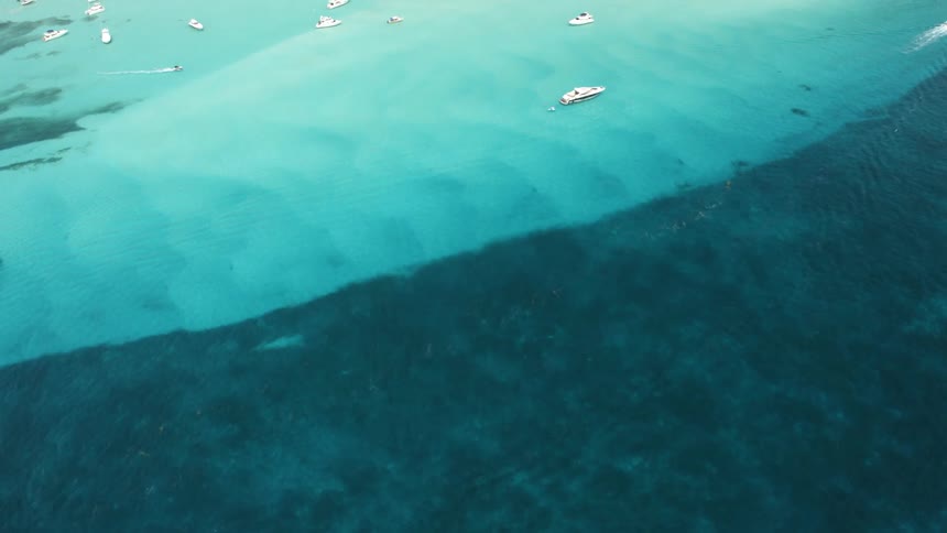 Boats sit in the blue ocean near the shoreline