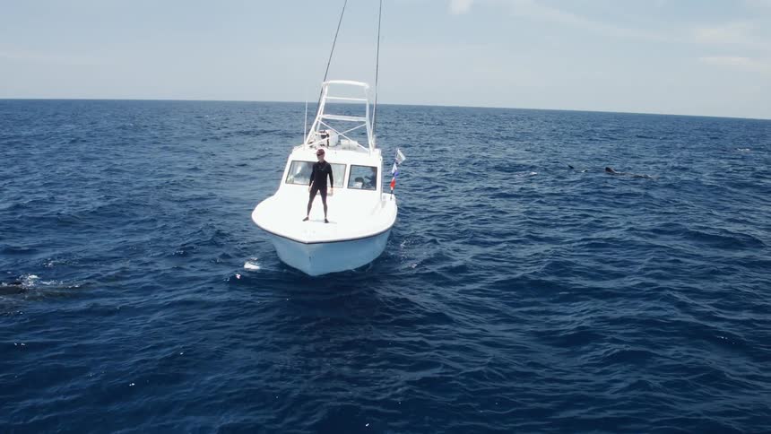 A man in a wet suit stands on a boat in the middle of an ocean
