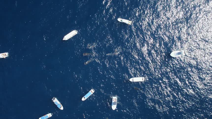 An aerial view of boats driving on the ocean is displayed
