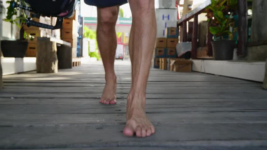 Man carrying a camera walks barefoot on the floorboard on a street
