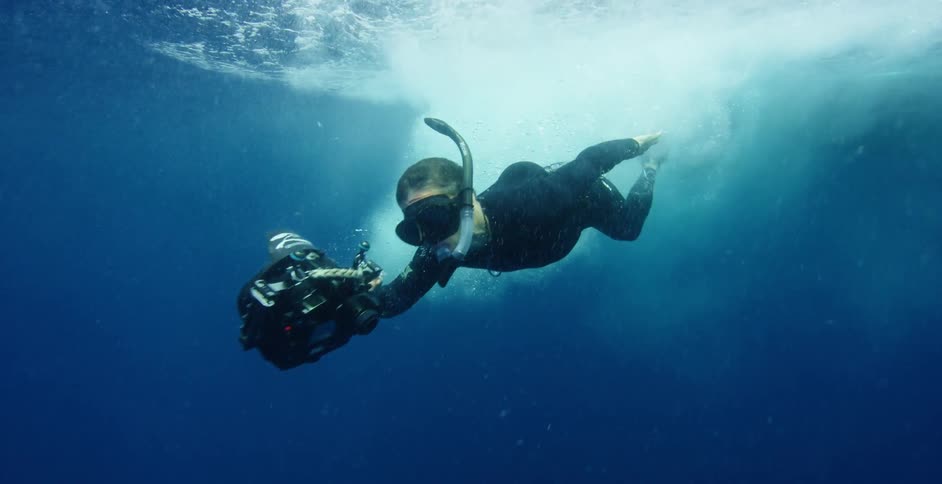 A man wearing a snorkel plunges into the ocean and begins to swim swiftly underwater
